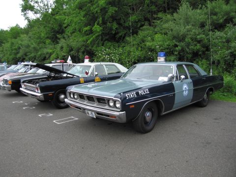 1991 Ford LTD Crown Victoria - two-tone State Police sedan with quad stacked headlights and a roof beacon parked among other vintage cruisers.