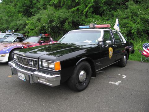 1991 Ford LTD Crown Victoria - black police sedan marked 154 with a Connecticut State Police door shield and roof light bar parked on asphalt.