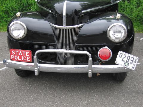 1991 Ford LTD Crown Victoria - chrome grille and front bumper of a black 1940s sedan bearing a red STATE POLICE plate and a vintage Connecticut tag.