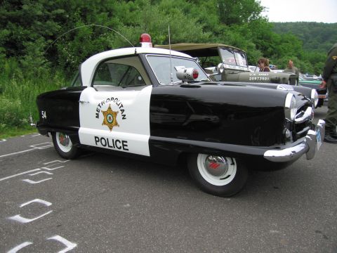 1991 Ford LTD Crown Victoria - tiny black-and-white Metropolitan Police compact car numbered 54 with a roof beacon parked at an outdoor show.