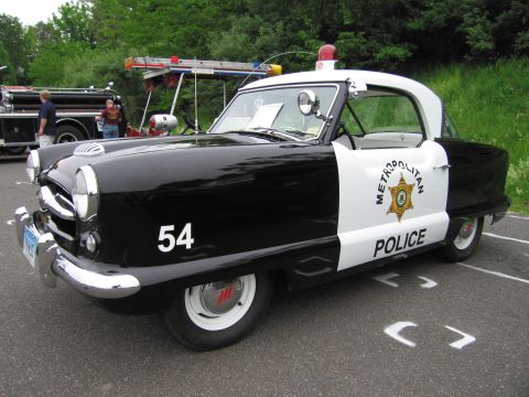 1991 Ford LTD Crown Victoria - Front quarter view of a small black-and-white Metropolitan Police compact car numbered 54 with a red roof beacon.