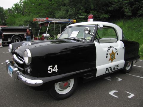 1991 Ford LTD Crown Victoria - small black-and-white Metropolitan Police compact numbered 54 parked beside a vintage fire truck at a show.