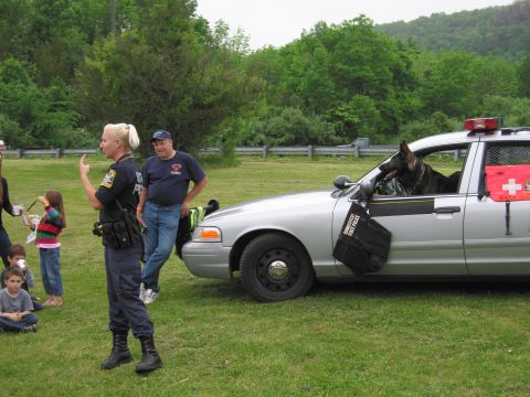 1991 Ford LTD Crown Victoria - officer addresses a small crowd at a K9 demonstration as a German Shepherd leans from a silver State Police cruiser.