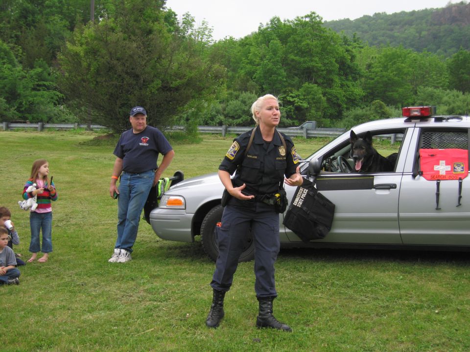 Female police officer gesturing in front of silver cruiser with K-9 dog in window