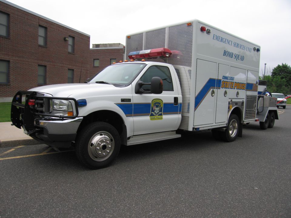 White Ford State Police Bomb Squad utility truck towing trailer by brick building