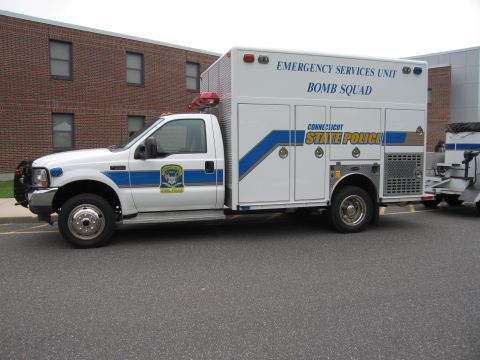 1991 Ford LTD Crown Victoria - Side profile of a white Connecticut State Police Bomb Squad Ford utility truck with blue striping and a red beacon, parked in a lot by a br…