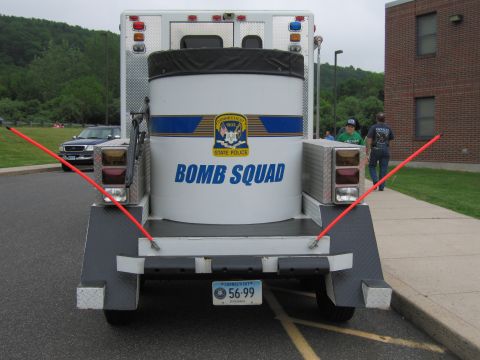 1991 Ford LTD Crown Victoria - Rear straight-on view of a large round bomb-containment vessel on a trailer behind a State Police Bomb Squad truck, with red support arms a…