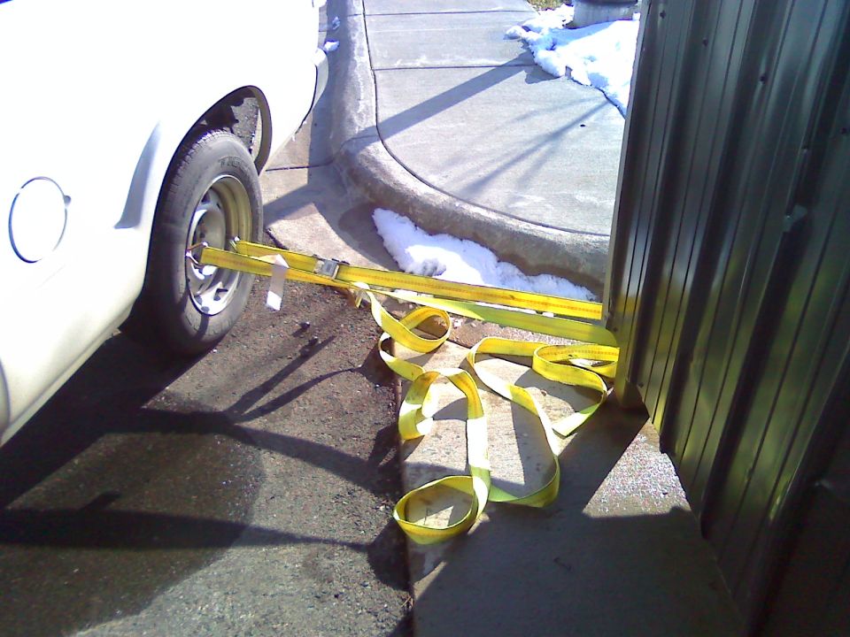 Side view of a white van with yellow tie-down straps securing the front wheel