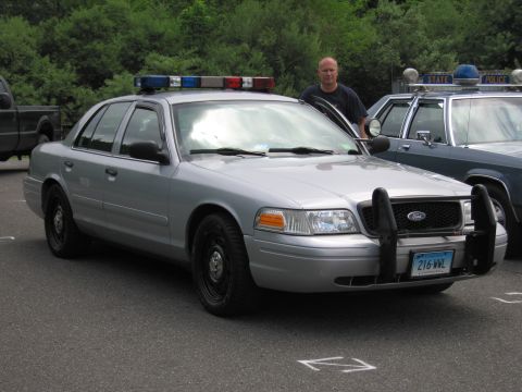 1991 Ford LTD Crown Victoria - silver Ford Crown Victoria police interceptor with roof light bar and push bumper parked beside a man at an outdoor show.