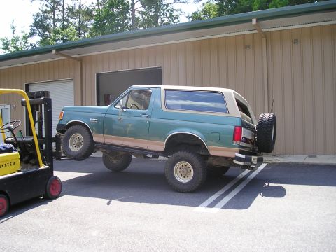 1989 Ford Bronco - A 1989 Ford Bronco is being lifted by a forklift next to a building.