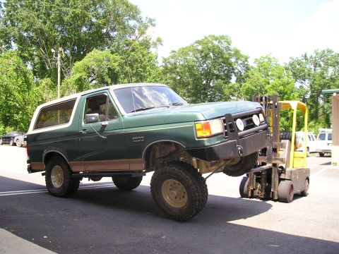 1989 Ford Bronco - A green Ford Bronco with a lifted suspension is being supported by a forklift.