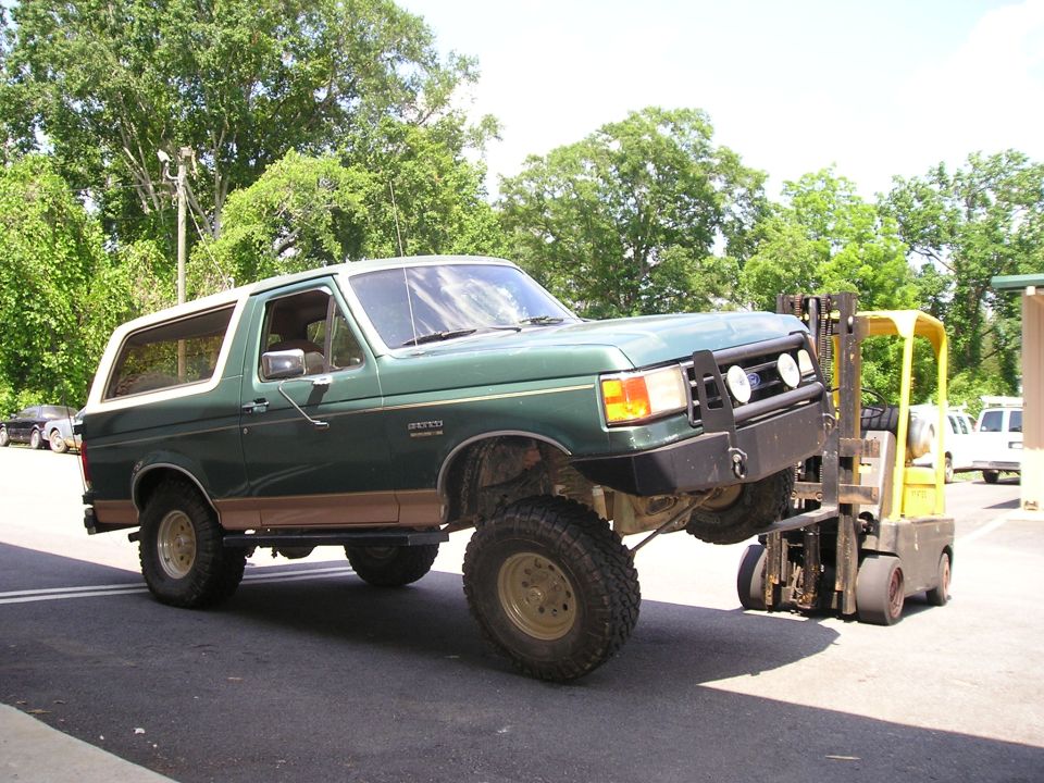 Green Ford Bronco with lifted suspension being held up by a yellow forklift
