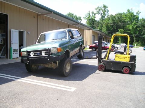 1989 Ford Bronco - A green 1989 Ford Bronco is being lifted by a yellow Hyster forklift in a parking lot.