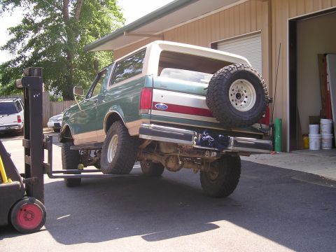 1989 Ford Bronco - A Ford Bronco is being lifted by a forklift outside a garage.