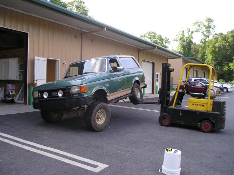 1989 Ford Bronco - A green 1989 Ford Bronco is being lifted by a yellow forklift outside a building.