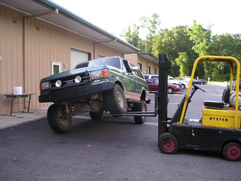 1989 Ford Bronco - A green and tan Ford Bronco with a black brush guard and driving lights is lifted off the pavement by a yellow Hyster forklift outside a ta…