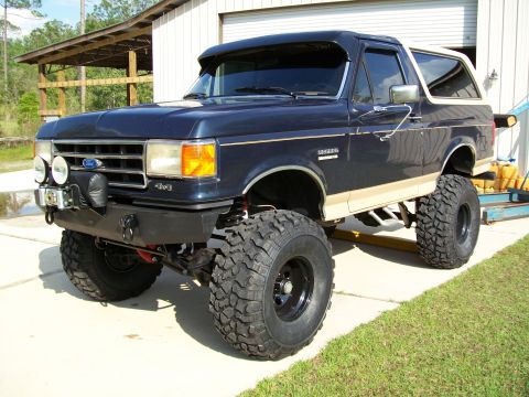 1990 Ford Bronco - This lifted 1990 Ford Bronco features a dark blue exterior with tan trim and aggressive off-road tires.