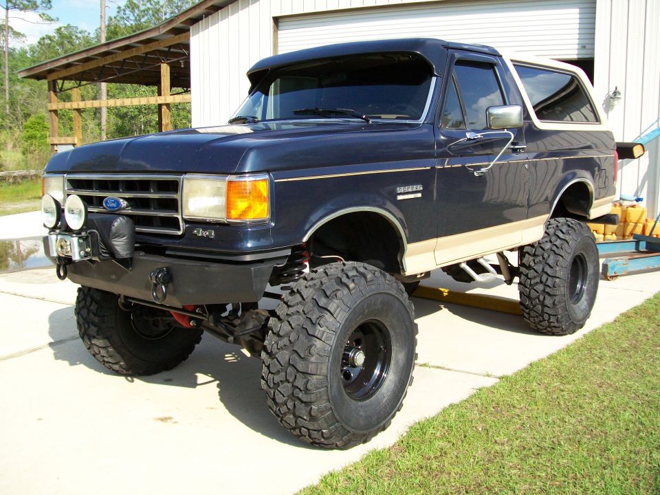 Lifted dark blue 1990 Ford Bronco with tan trim and large off-road tires