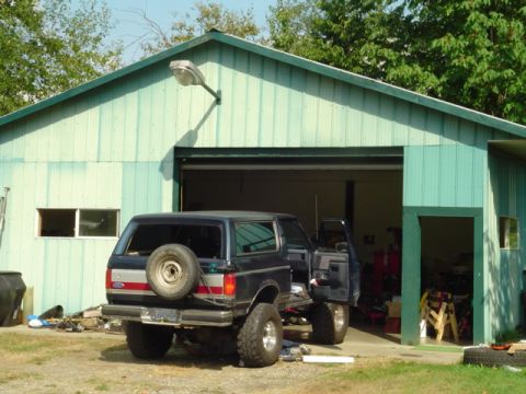 1990 Ford Bronco - A dark blue Ford Bronco is parked outside a green garage with its doors open.