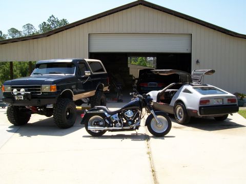 1990 Ford Bronco - Three distinct vehicles are parked outside a garage on a sunny day.