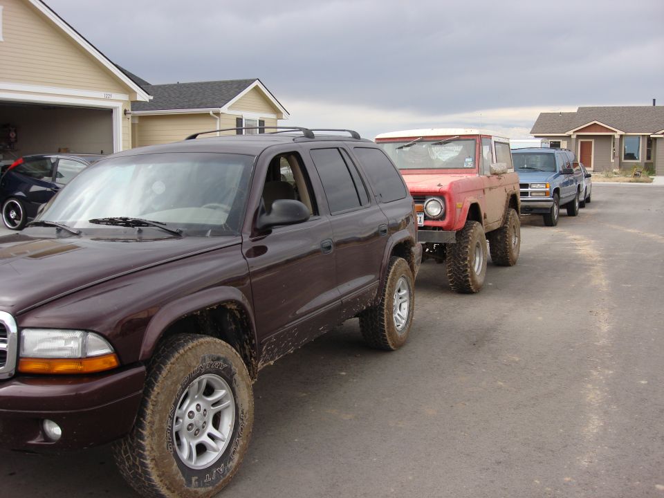 Red lifted early Ford Bronco parked between a maroon Durango and blue SUV on a residential street