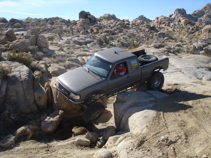 Gray pickup truck crawling over rocks on a trail. Driver is visible