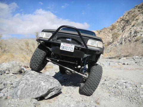 1997 Ford Ranger - A modified 1997 Ford Ranger navigates a rocky desert terrain with its front wheels on large boulders.