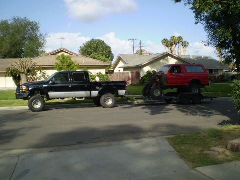 1969 Ford F-250 - A black Ford F-250 Super Duty tows a red Ford Bronco on a trailer down a suburban street.