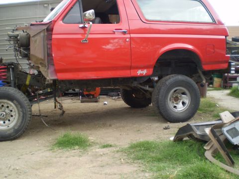 1969 Ford F-250 - This red Ford Bronco is undergoing repairs or modifications, with its front end disassembled and lifted.