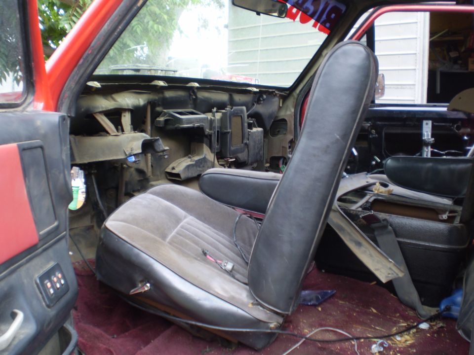 Interior of a red truck cab with disassembled dashboard, worn seats, and red carpet
