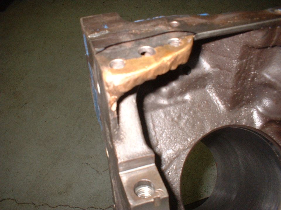 Close-up of engine block corner with bronze brazed repair near bolt holes and a cylinder bore visible