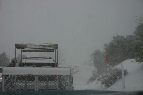 1991 Ford Bronco - A golf cart tows a trailer through a snowstorm, with other vehicles barely visible on the road ahead.