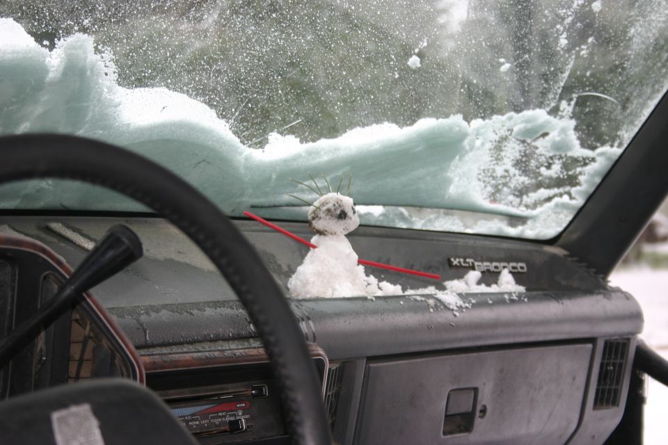 Dashboard of a 1991 Ford Bronco with a small snowman on the dash and snow on the windshield