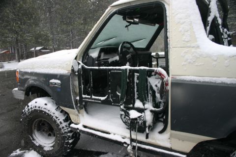 1991 Ford Bronco - The interior and side of a 1991 Ford Bronco are visible, covered in snow, with the driver's door open.