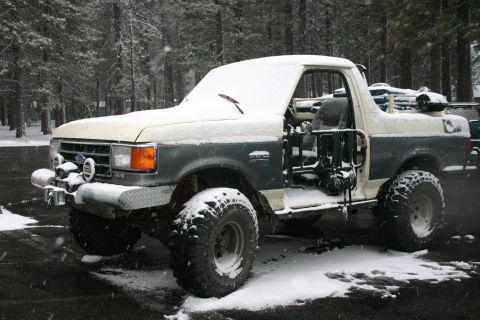 1991 Ford Bronco - A two-tone Ford Bronco sits parked in the snow, its doors open.