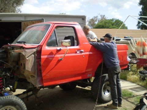 1969 Ford F-250 - Two men work on a red pickup truck that is missing its front end.