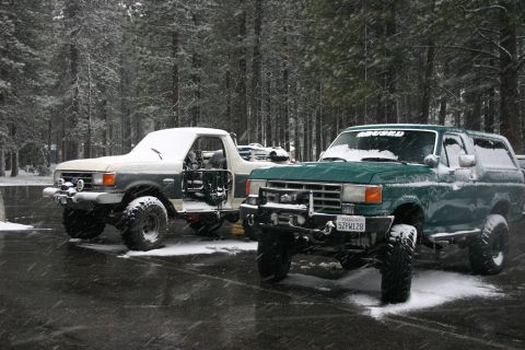 1991 Ford Bronco - Two Ford Broncos, one green and one white, parked in a snowy forest setting.