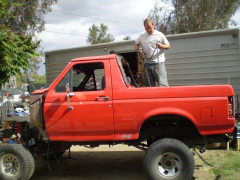 1969 Ford F-250 - Red pickup truck undergoing work, with front end disassembled and a man handling chains in the bed.