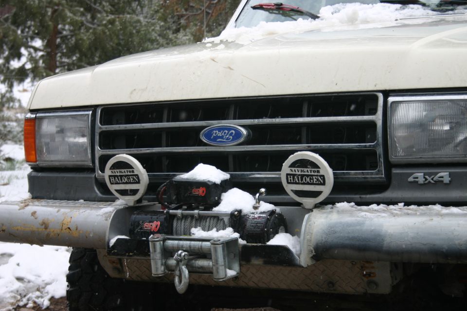 Front of a white Ford Bronco with a winch and halogen lights, covered in snow