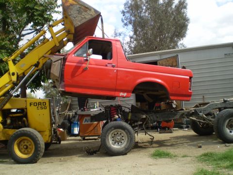 1969 Ford F-250 - Red Ford pickup truck body being removed from its chassis by a loader.