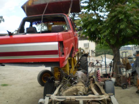 1969 Ford F-250 - A red truck cab and chassis, a silver stripe, is suspended and undergoing work.