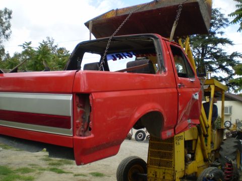 1969 Ford F-250 - A red Ford pickup truck cab is being lifted by a yellow loader. The truck's bed is missing.