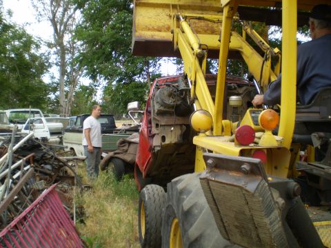 1969 Ford F-250 - A backhoe is lifting a red truck cab in a junkyard setting with multiple other vehicles present.