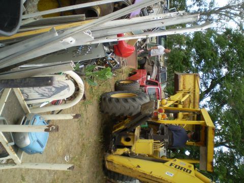 1969 Ford F-250 - A collection of vehicles and scrap metal are piled up in a yard, with a yellow front loader in the foreground.