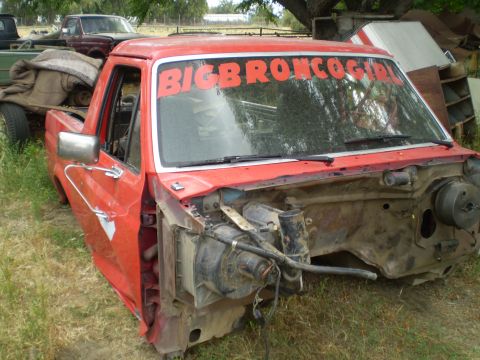 1969 Ford F-250 - A red pickup truck cab sits in a yard with other vehicles, its front end removed and a custom decal on the windshield.