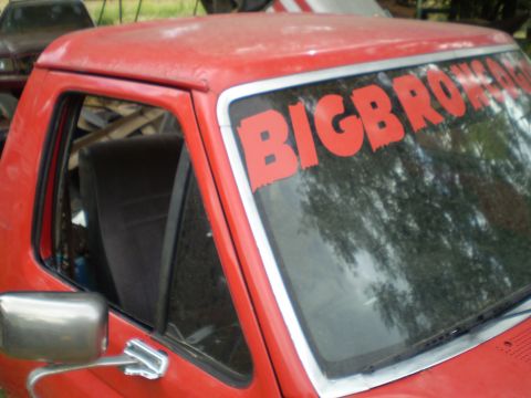 1969 Ford F-250 - Red pickup truck cab with 'BIGBRO' lettering on the windshield. Another vehicle is visible in the background.