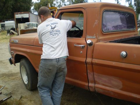 1969 Ford F-250 - A man is seen working on the interior of a vintage orange pickup truck, possibly a Ford F-Series from the late 1960s.