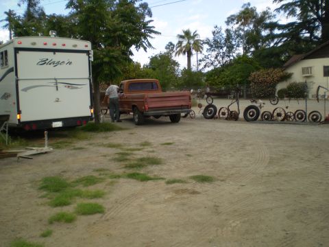 1969 Ford F-250 - An orange pickup truck and a white trailer are parked in a yard with decorative wheels on a fence.