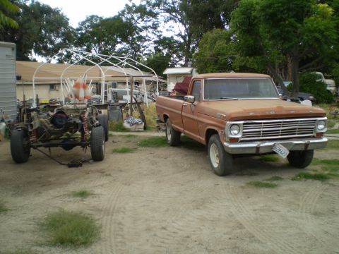 1969 Ford F-250 - A rusty Ford pickup sits beside a disassembled vehicle chassis in a yard.