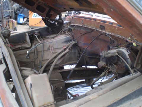 1969 Ford F-250 - The engine bay of a weathered vehicle shows extensive rust and disarray, with various hoses and wires exposed.